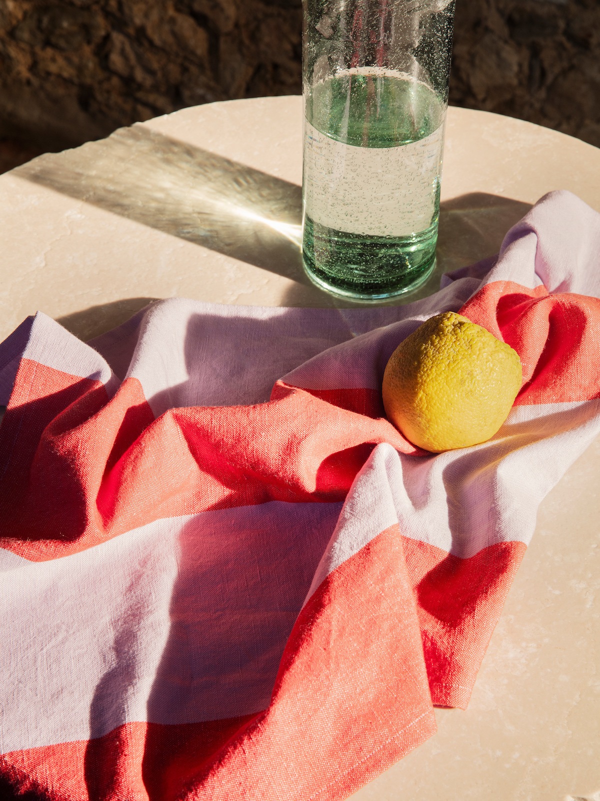 Gestreiftes Küchentuch in rosa und rot, darauf eine Zitrone. Dahinter steht eine Glaskaraffe.