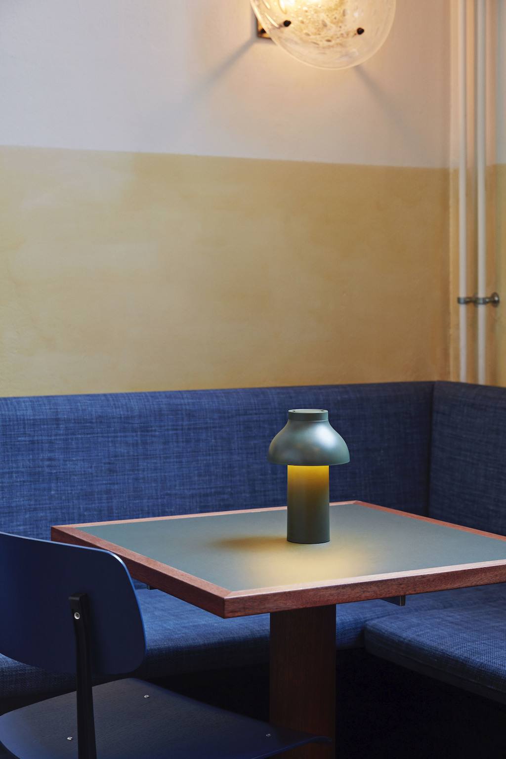 Olivgrüne PC Portabel Outdoorleuchte von HAY auf einem Tisch mit blau-bezogener Sitzecke.