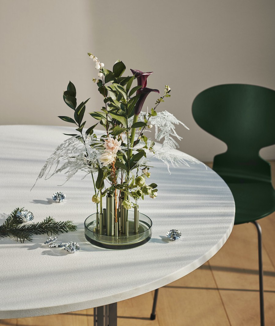 Ikeru Vase von Jaime Hayon für Fritz Hansen, gespickt mit Blumen auf einem Tisch, im Hintergrund ein grüner Ant Stuhl. 
