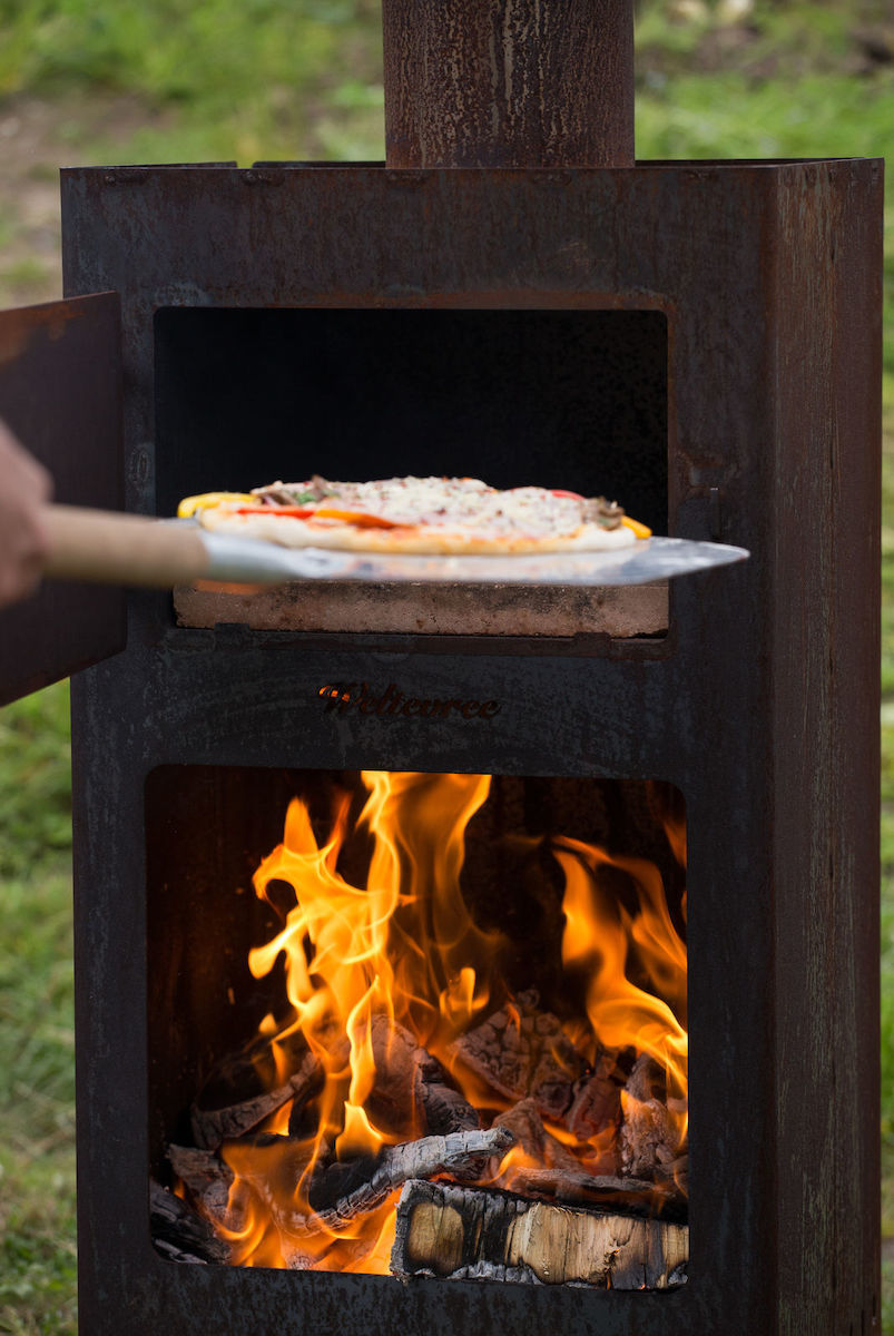 Eine Pizza wird in den Outdooroven geschoben. Die untere Klappe ist geöffnet und Flammen sind zu sehen. 
