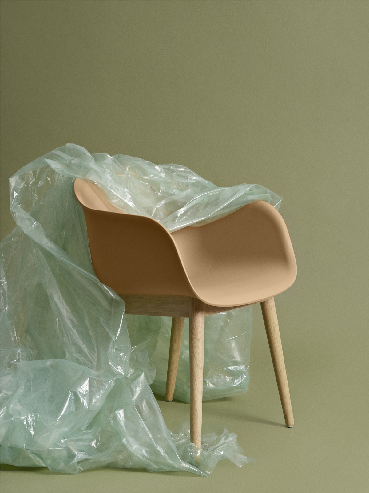 Muuto Fiber Chair. Modell mit Armlehnen und Holzbasis, Kunststofffolie hängt halb über dem Stuhl. 