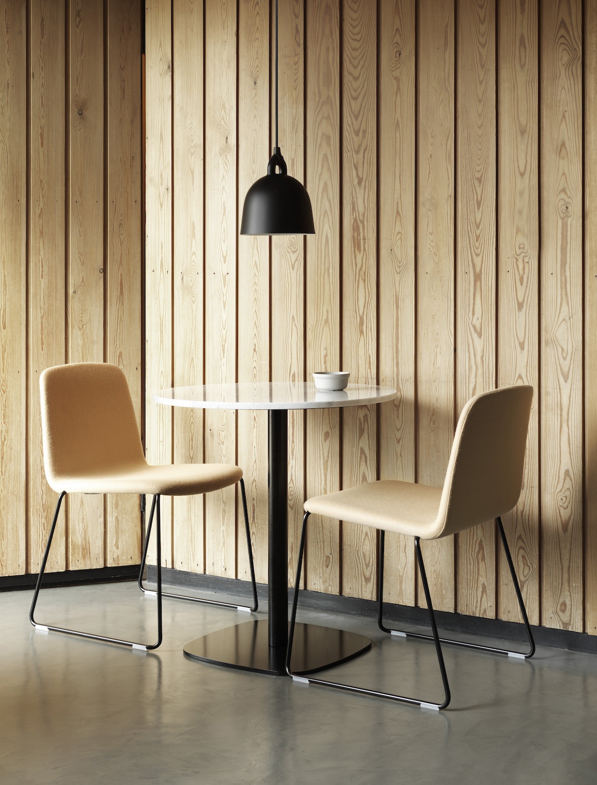 Bistrotisch Form von Normann Copenhagen und zwei Stühle vor einer holzvertäfelten Wand. 