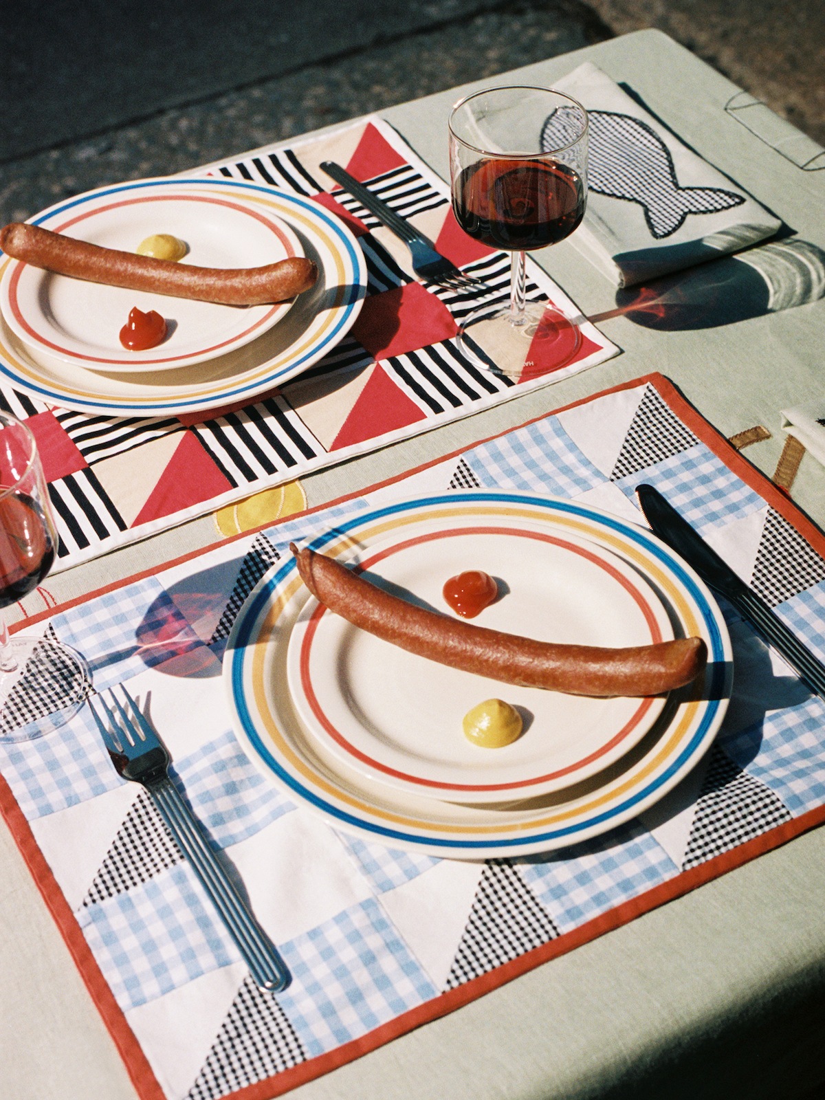Zwei Tischsets mit Tellern und je einer Wiener Wurst, daneben jeweils ein klecks Ketchup und Senf