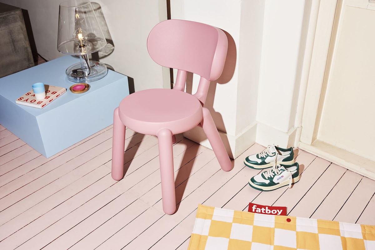 Rosa Stuhl auf rosa gestrichenem Holzboden, rechts steht ein Paar Turnschuhe.