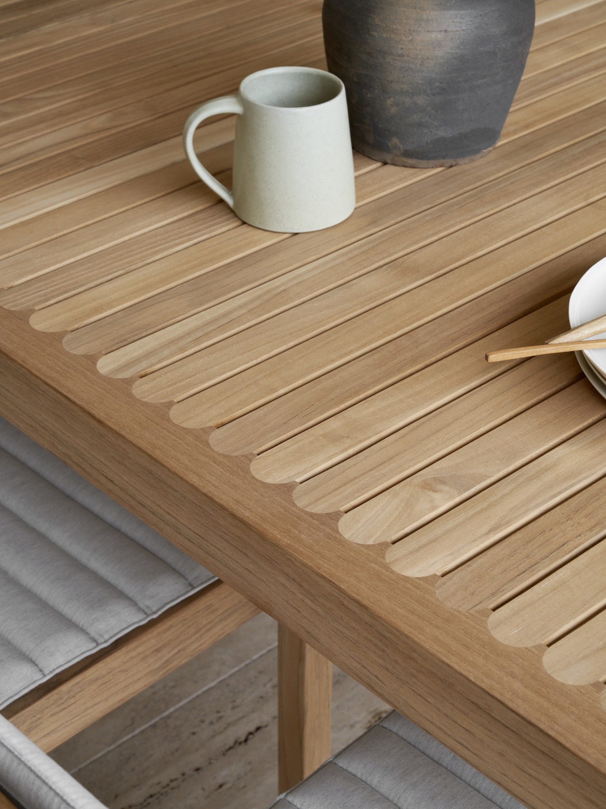 Tischplatte aus Teakleisten mit kleinem Abstand, darauf steht eine Tasse aus heller Keramik. 