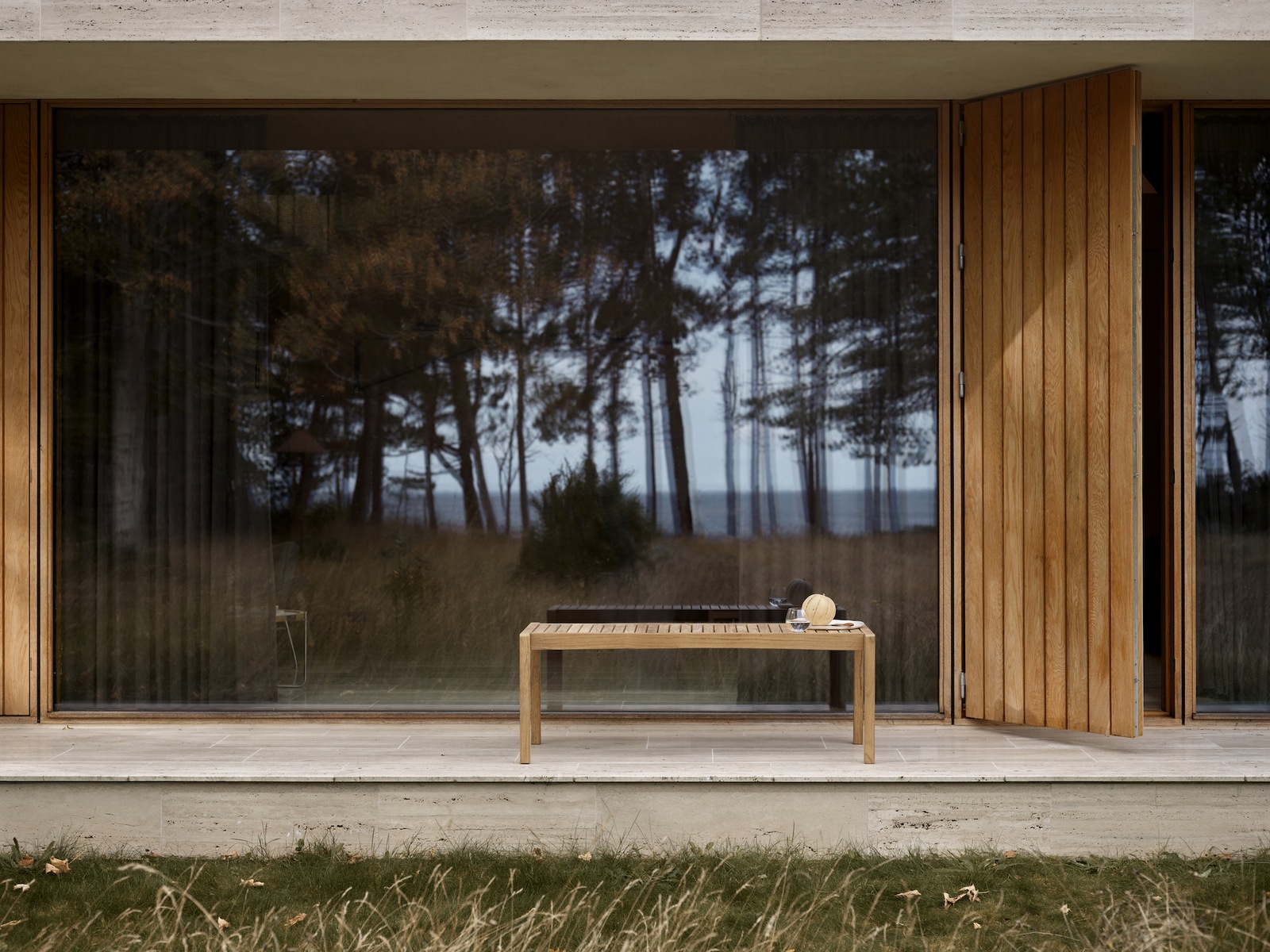 Exteriorshot: eine Holzbank ohne Rückelehne steht vor einem Bodentiefen Panaoramafenster.