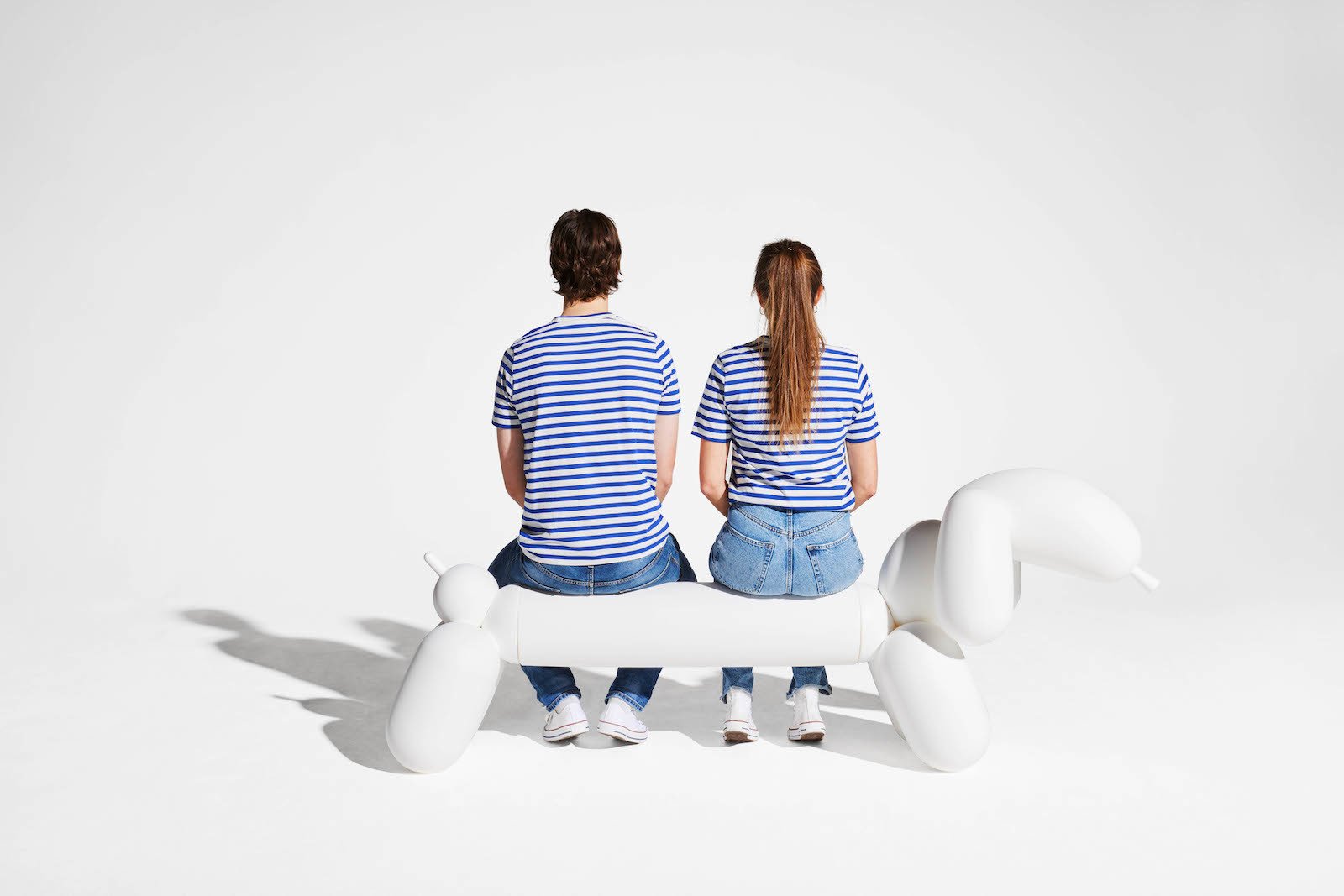 Zwei Menschen in gestreiften T-Shirts sitzen auf einer weißen Bank in Dackelform. 