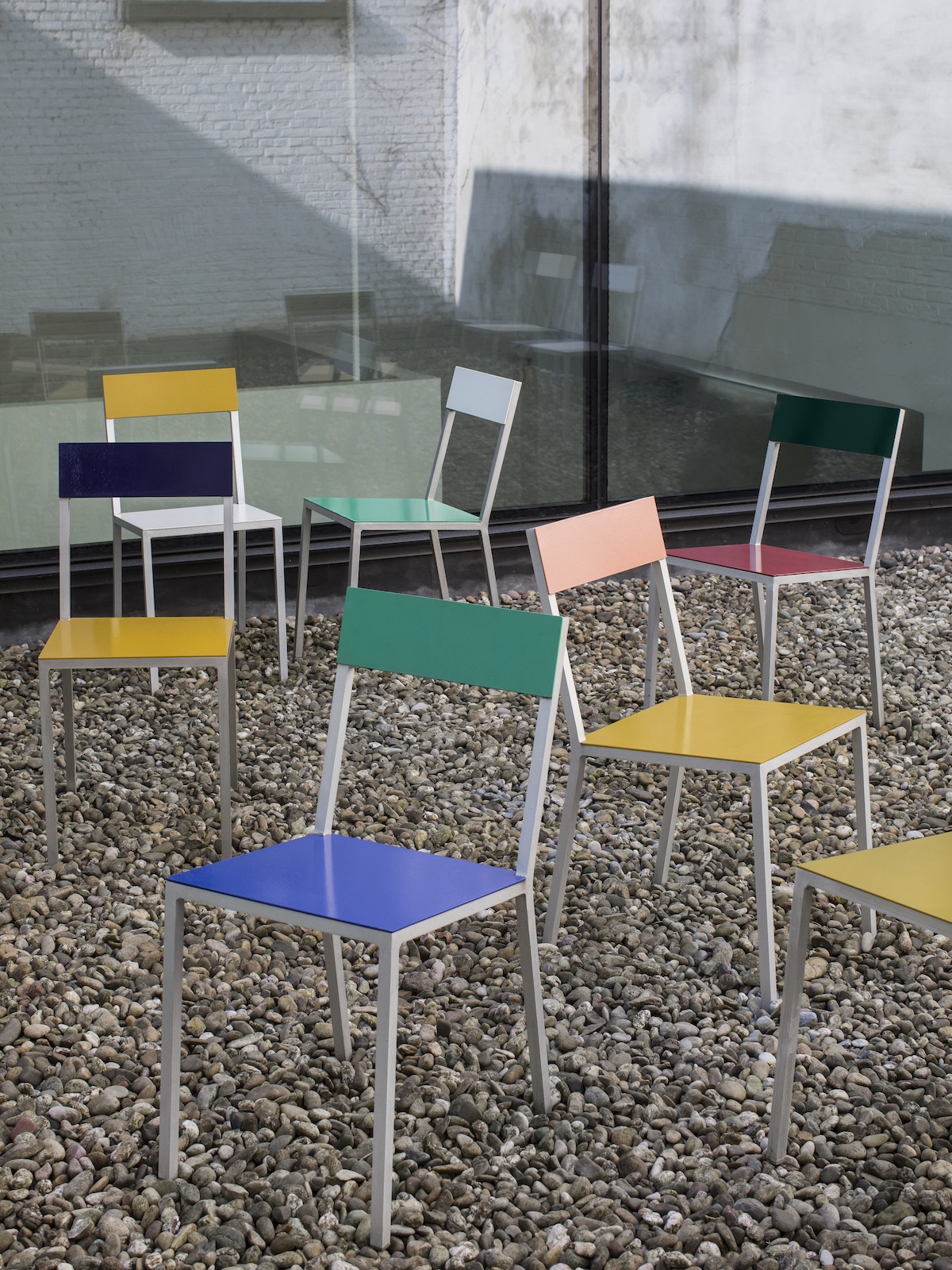 Kiesfläche, auf der viele bunte Alu Chairs von Muller van Severen stehen. 