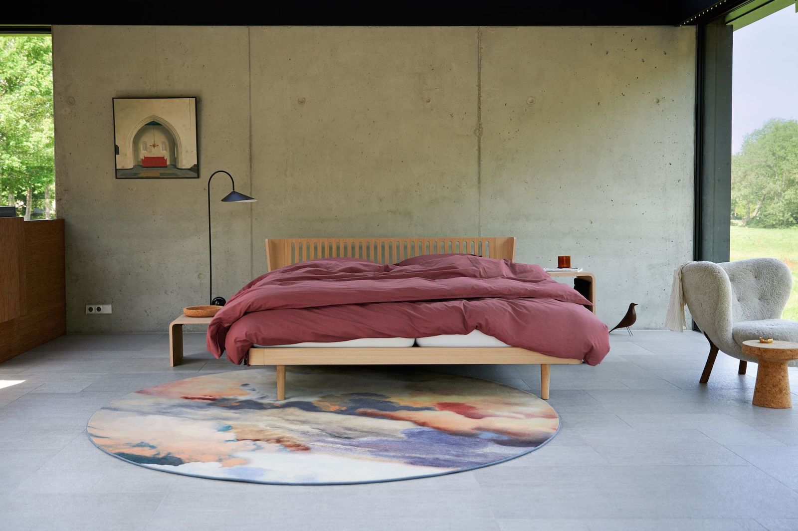 Auping Noa Bett mit Burgunderfarbener Bettwäsche steht vor einer rauen Betonwand